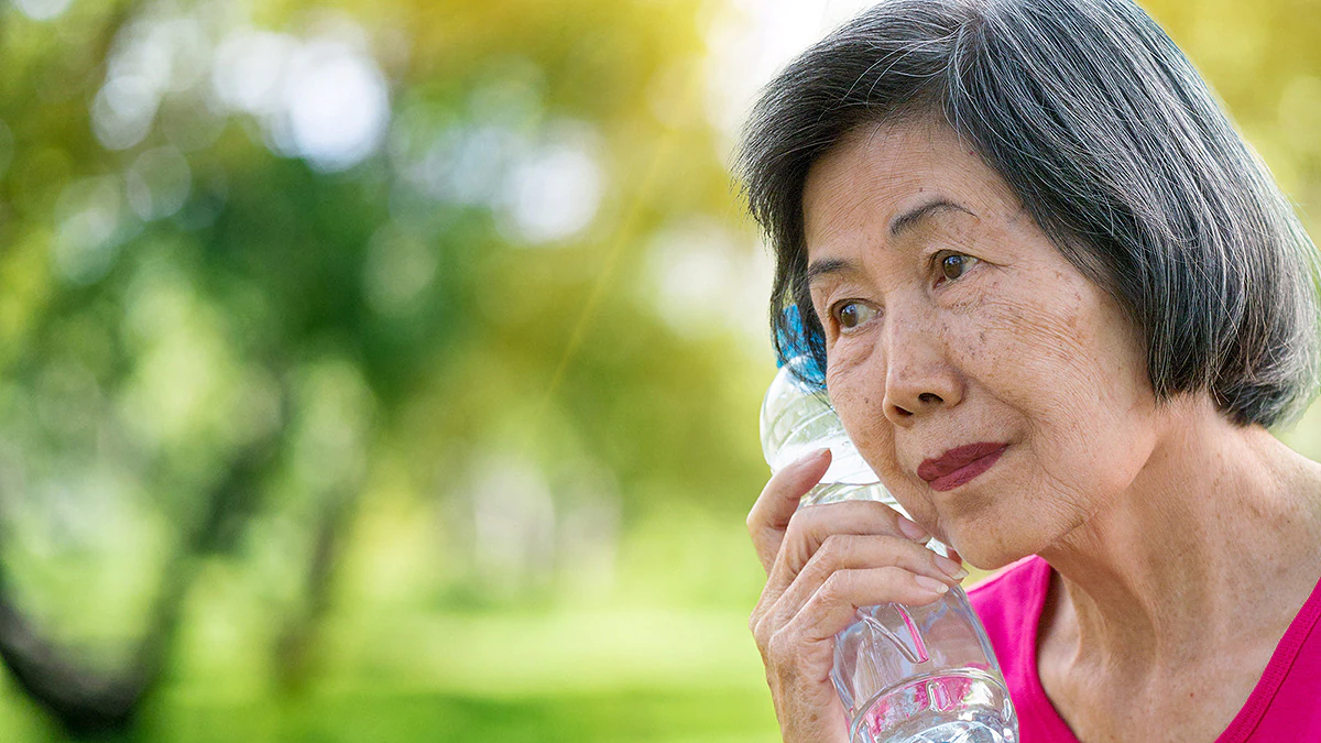Woman with Water Bottle Asian woman holds plastic bottle of water to her face to cool.