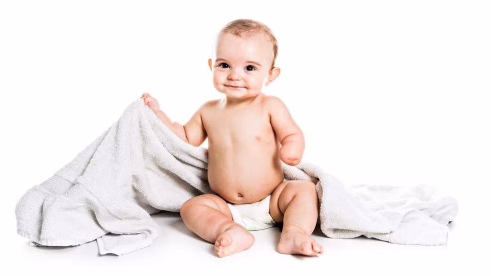 Happy baby with a missing hand from a congenital limb deficiency sitting on a blanket.