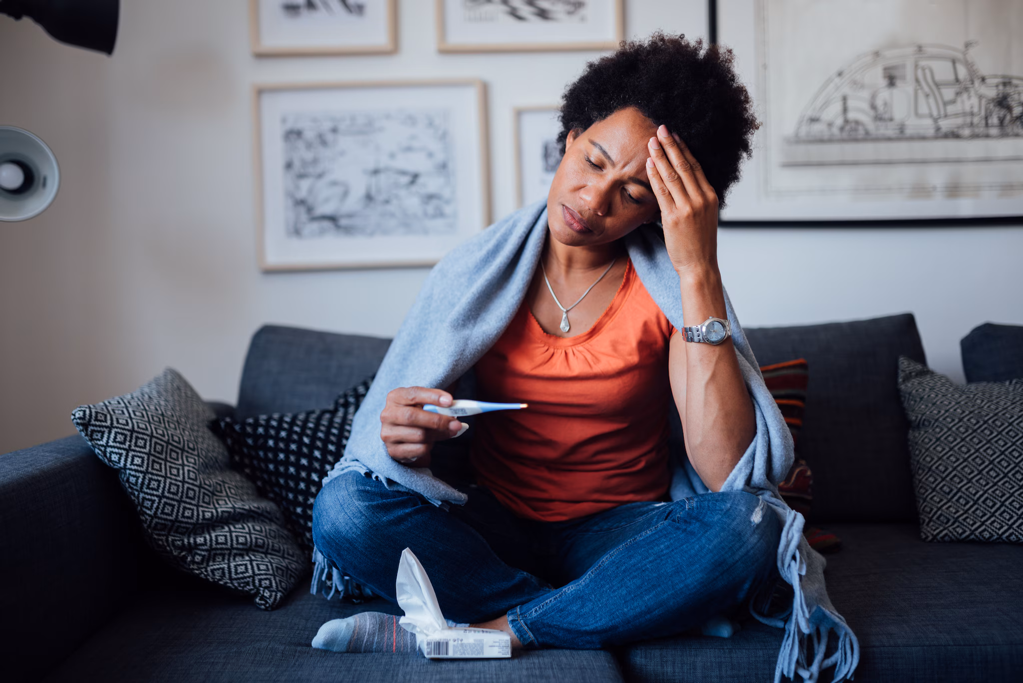 Most blastomycosis infections affect the lungs. A woman sitting on a sofa holding her head and checking the thermometer