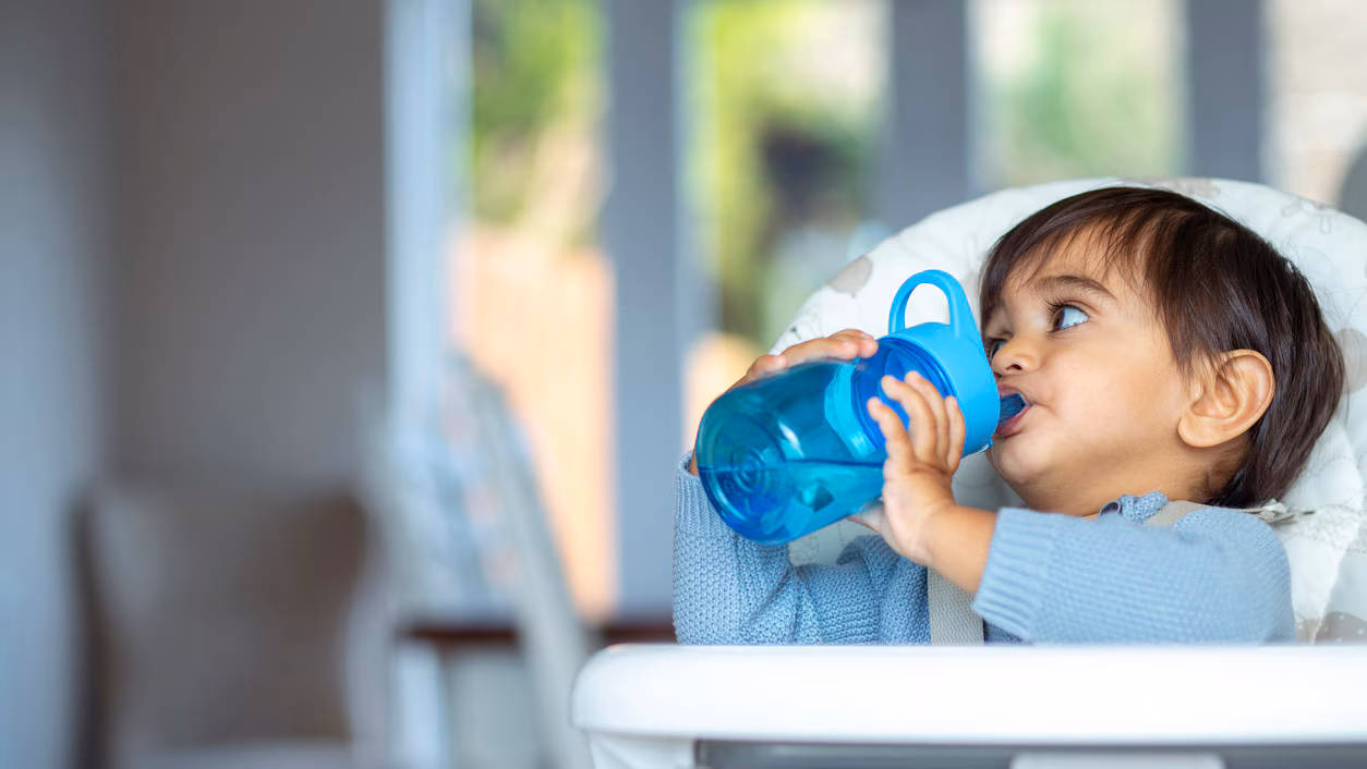 Toddler drinking from cup A toddler sits in a high chair and drinks from a cup.