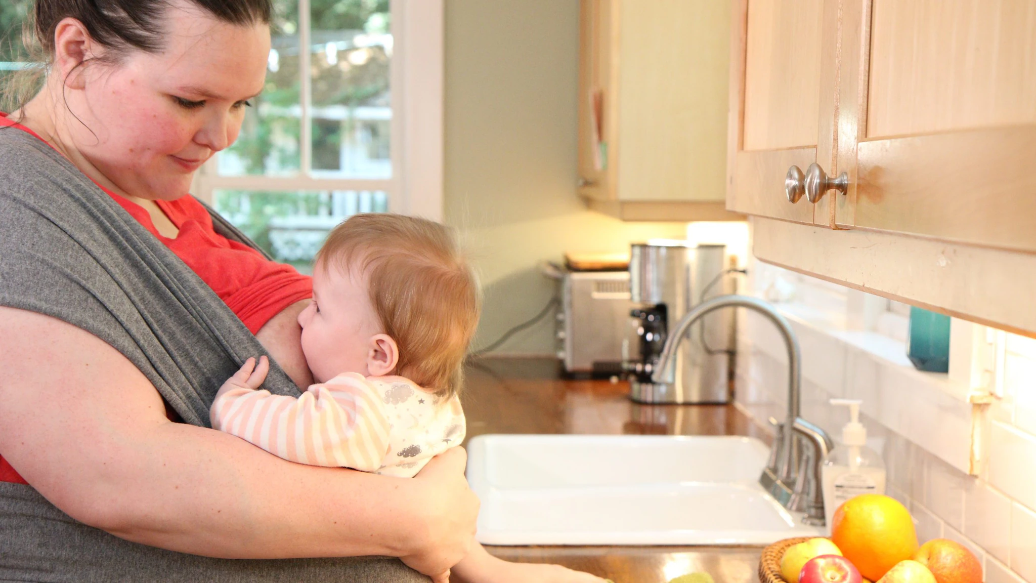 Woman breastfeeds at kitchen counter Woman breastfeeds while standing at the kitchen counter.
