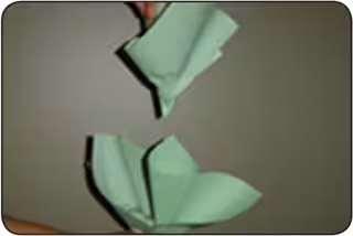 A person folds sheets of green paper to form a paper cabbage