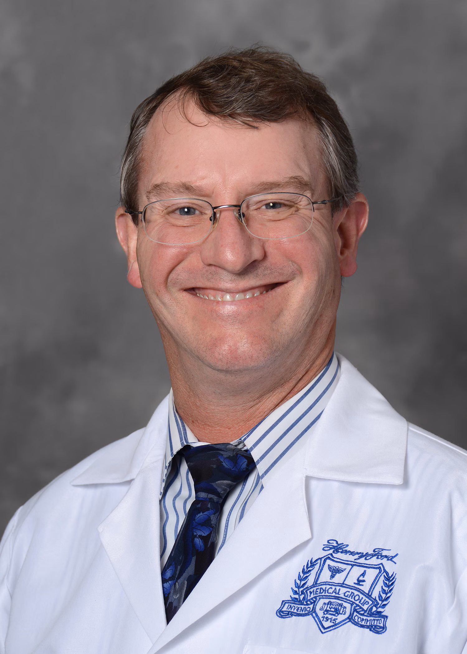 tuthill Dr. Tuthill's headshot. He is wearing a white lab coat, striped button up dress shirt, and blue tie.