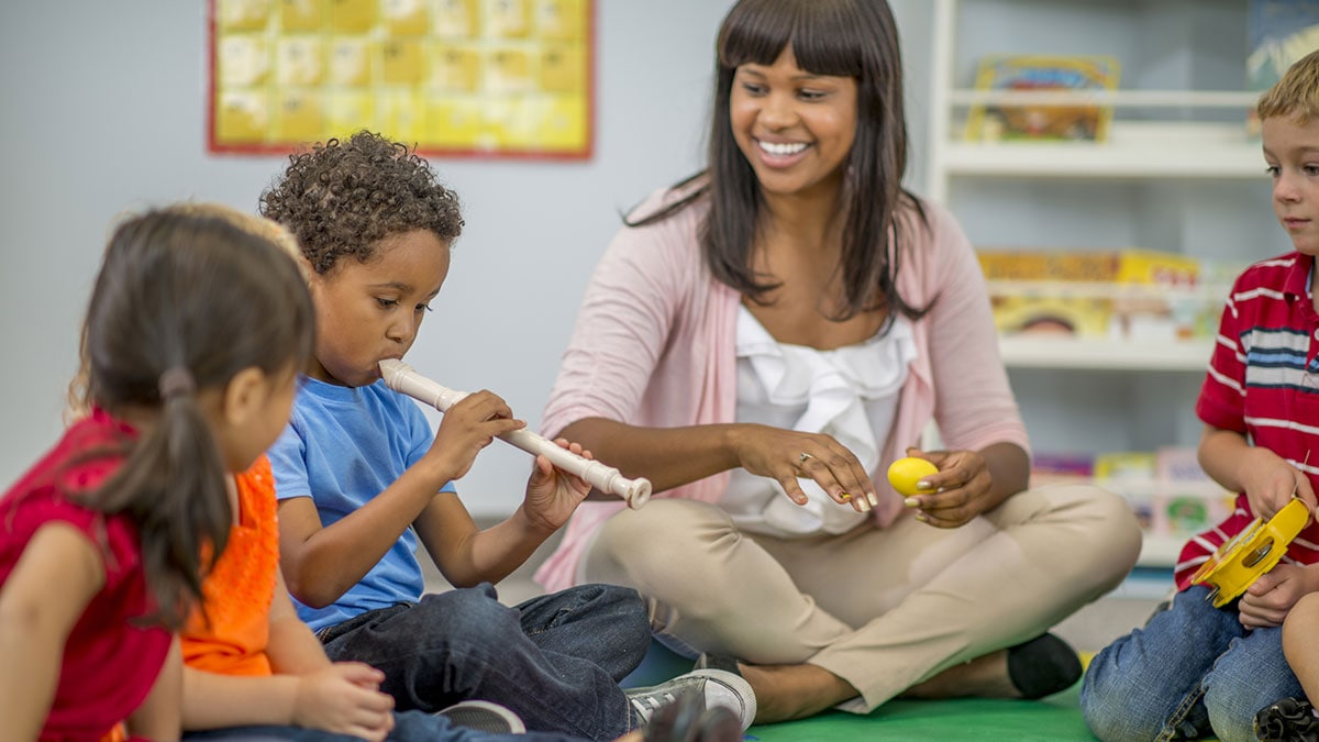Teacher with young kids Teacher sitting in a circle with elementary age children playing the recorder.