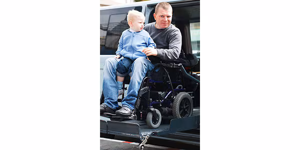 man-in-wheelchair-holding-child-600x300 A man is using a wheelchair and holding a child on his lap.