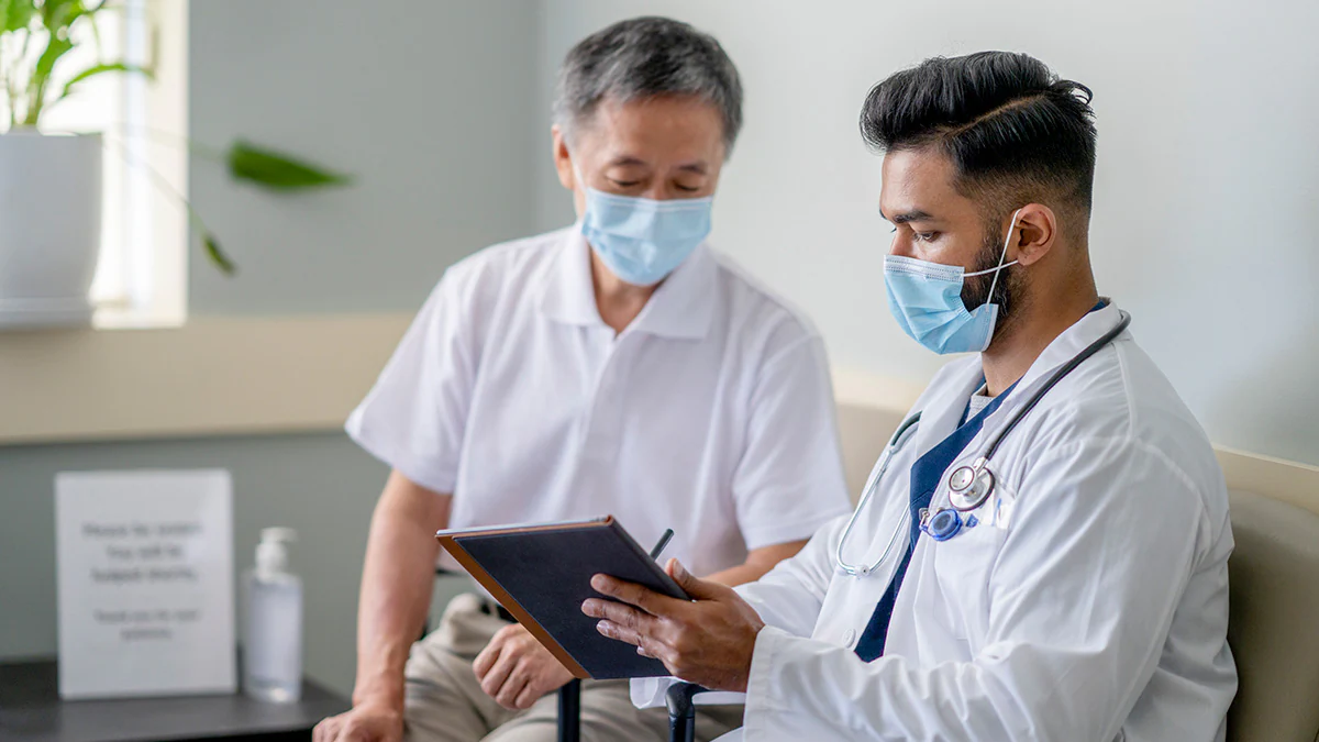 Patient and doctor wearing masks going over medical chart Patient and doctor wearing masks going over medical chart