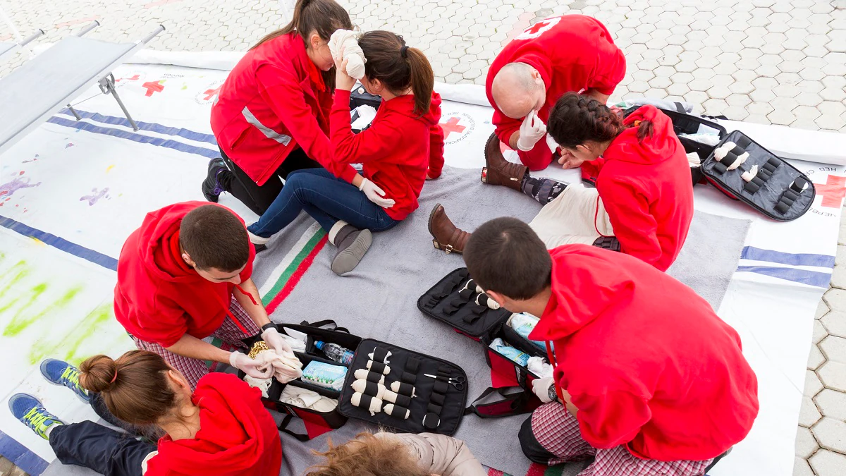 Red Cross Youth Organization Group of first aid trainees practicing emergency care outdoors.