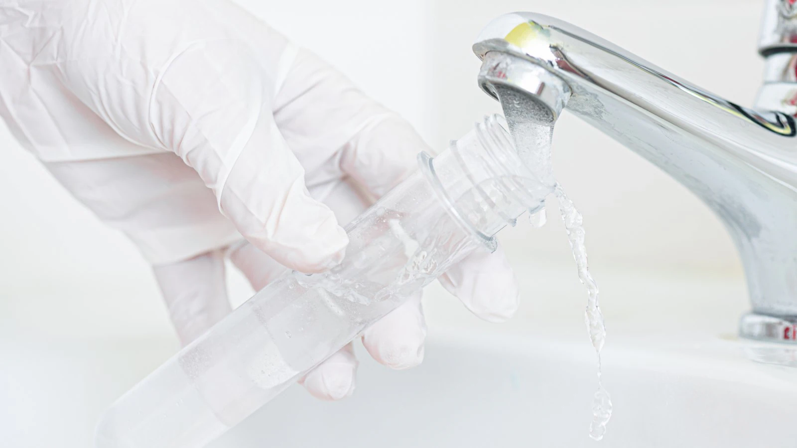 Water testing Gloved hand holding a test tube under a running faucet to collet water