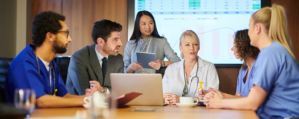 How to Implement ELR Team meeting between various staff members including physicians, patient care team, and hospital administration showing graphs with data on a screen in background.