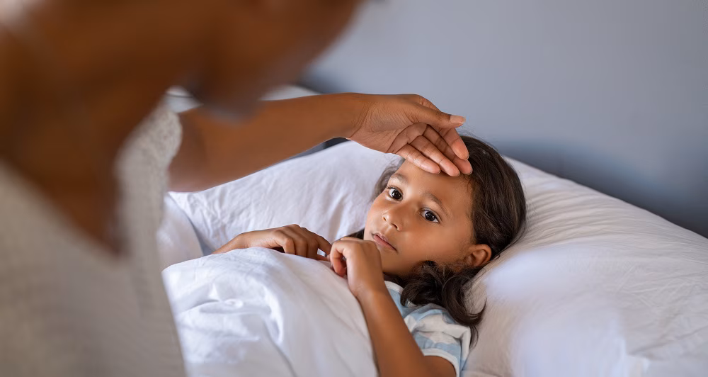 Parent uses hand to check temperature of child sick in bed. Parent uses hand to check temperature of child sick in bed.