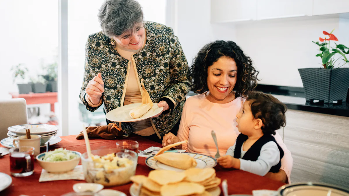 — title missing — A family sitting at a table with tortillas and tamales on their plates.