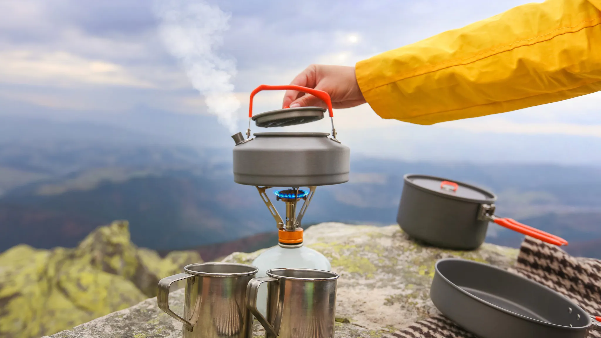 — title missing — Hiker boiling water in a kettle with mountains in the background