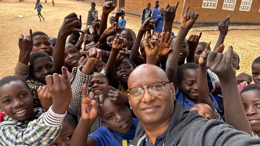Malawi_Epidemiology-Polio_Photo Man takes a photo with a group of children outside of a school building.