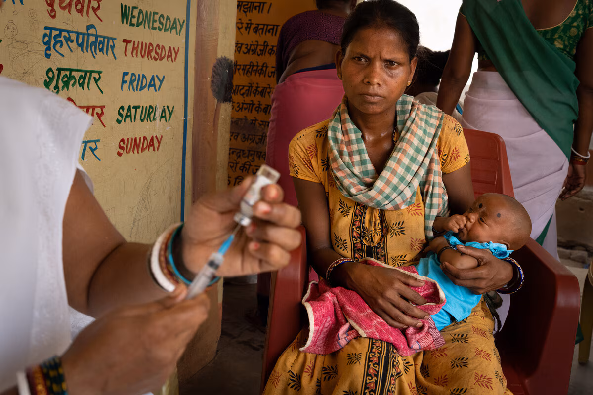 A woman holds her infant as a nurse prepares to administer a vaccine to the baby during Village Health and Nutrition Day
