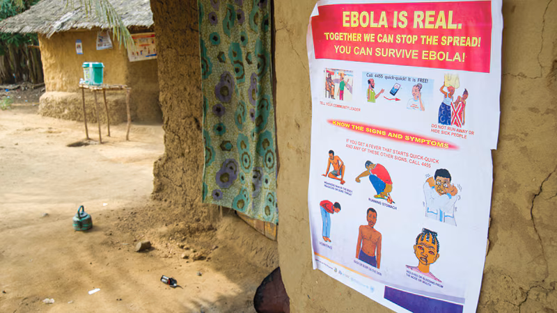 Liberia Poster An Ebola awareness poster on a mud wall in a rural setting, detailing symptoms and prevention.