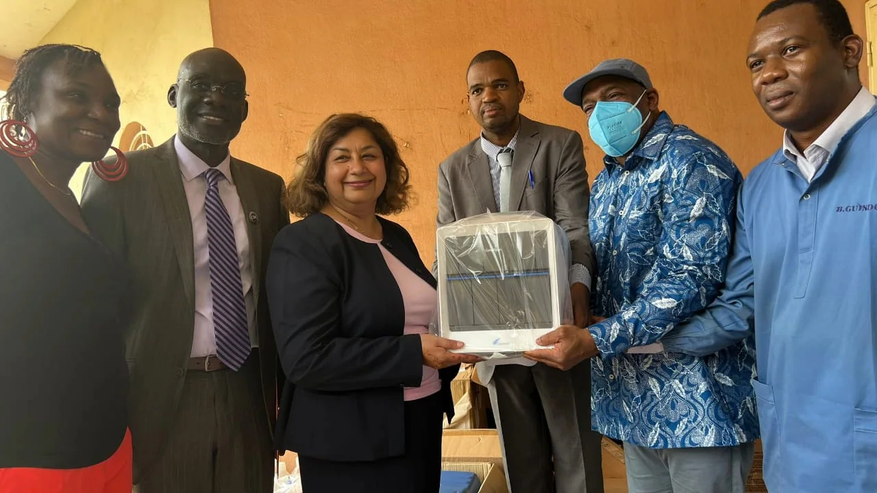 Mali Lab Visit Six individuals pose for a photo while holding a piece of laboratory equipment.