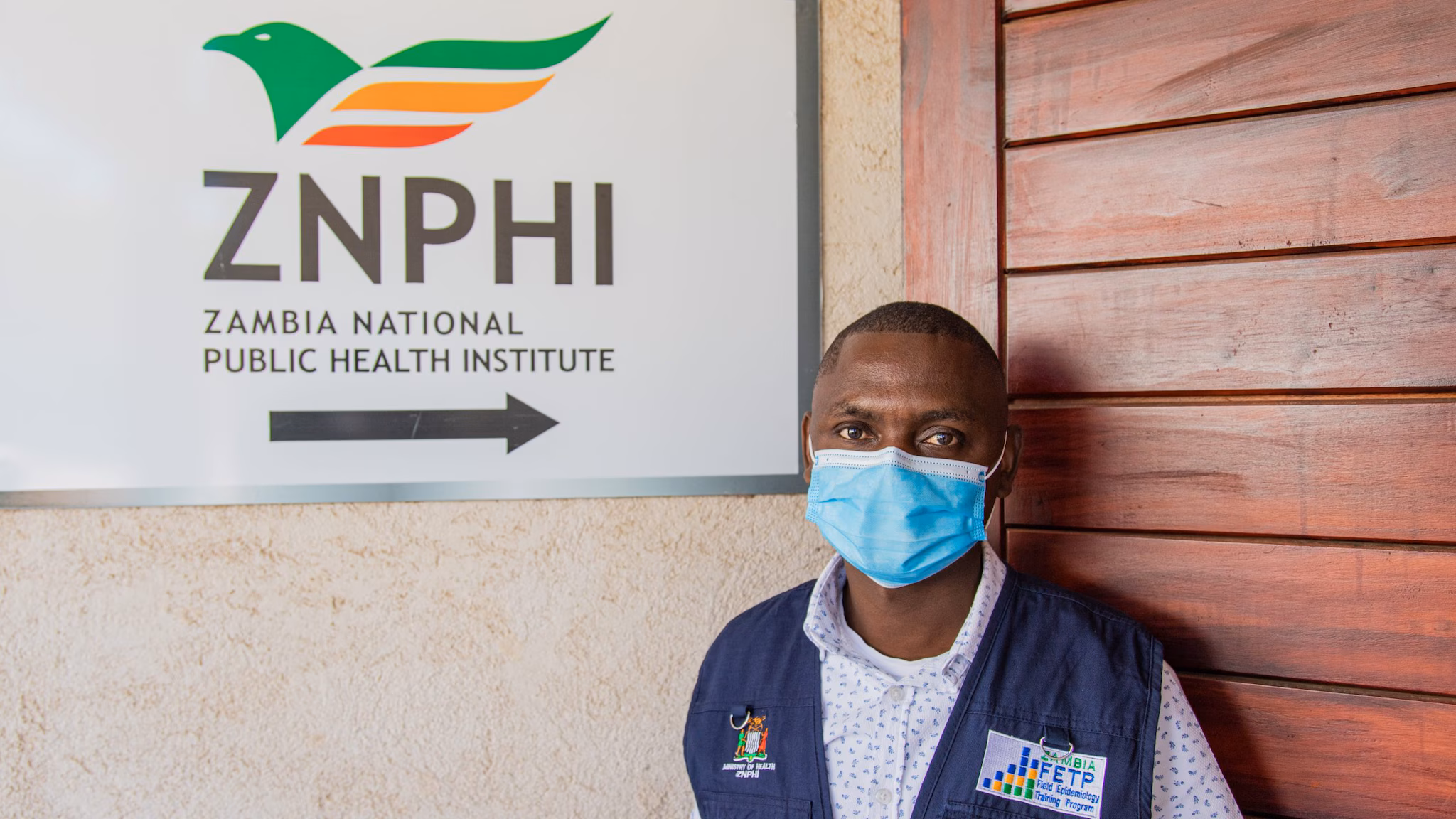 — title missing — Dr. Dabwitso Banda stands outside of the Zambia National Public Health Institute with Mask on.