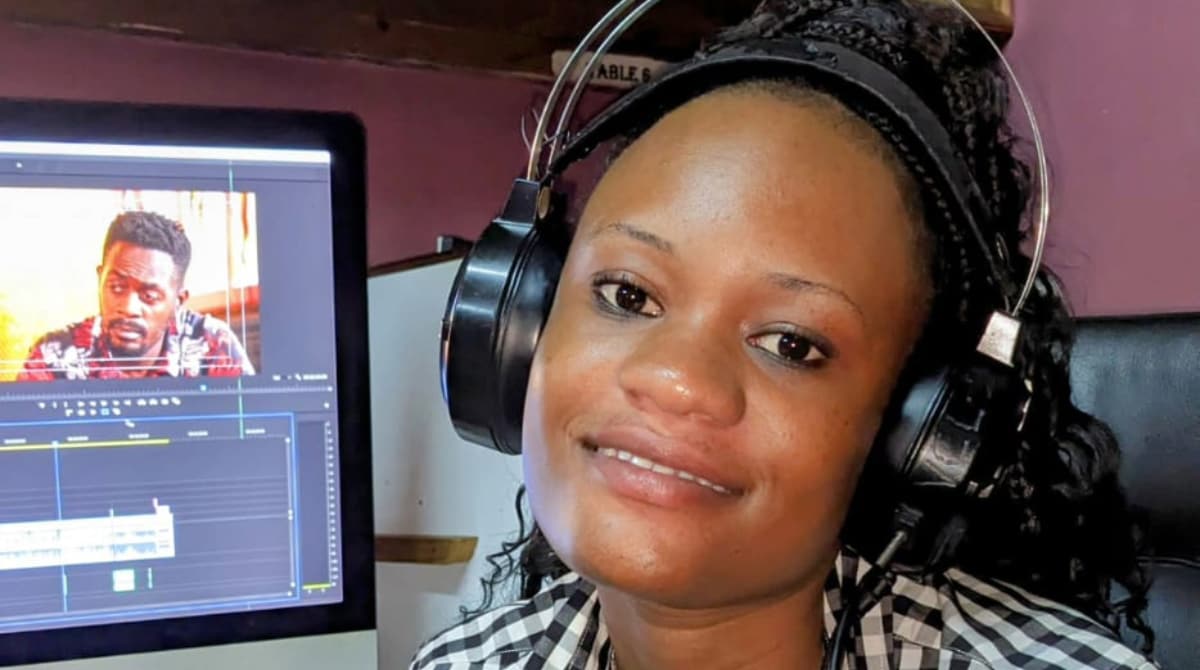 — title missing — A woman wearing headphones sits in front of a computer screen that is displaying video editing software.