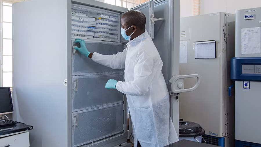 — title missing — An gloved and masked individual stands in front of an open freezer to place samples inside.