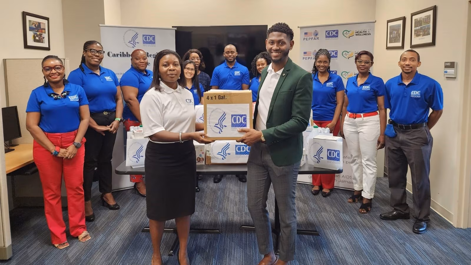 Group of 10 people, two stand at the front holding a box with the CDC/HHS logo