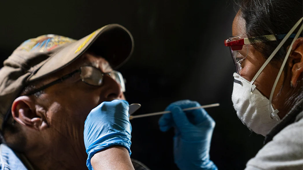 CDC Central America A person wearing a mask and gloves holds a swab in another person's mouth to collect an oral sample.