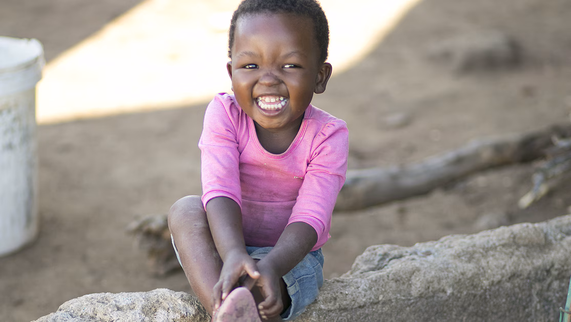 A girl in a pink shirt smiles while sitting.