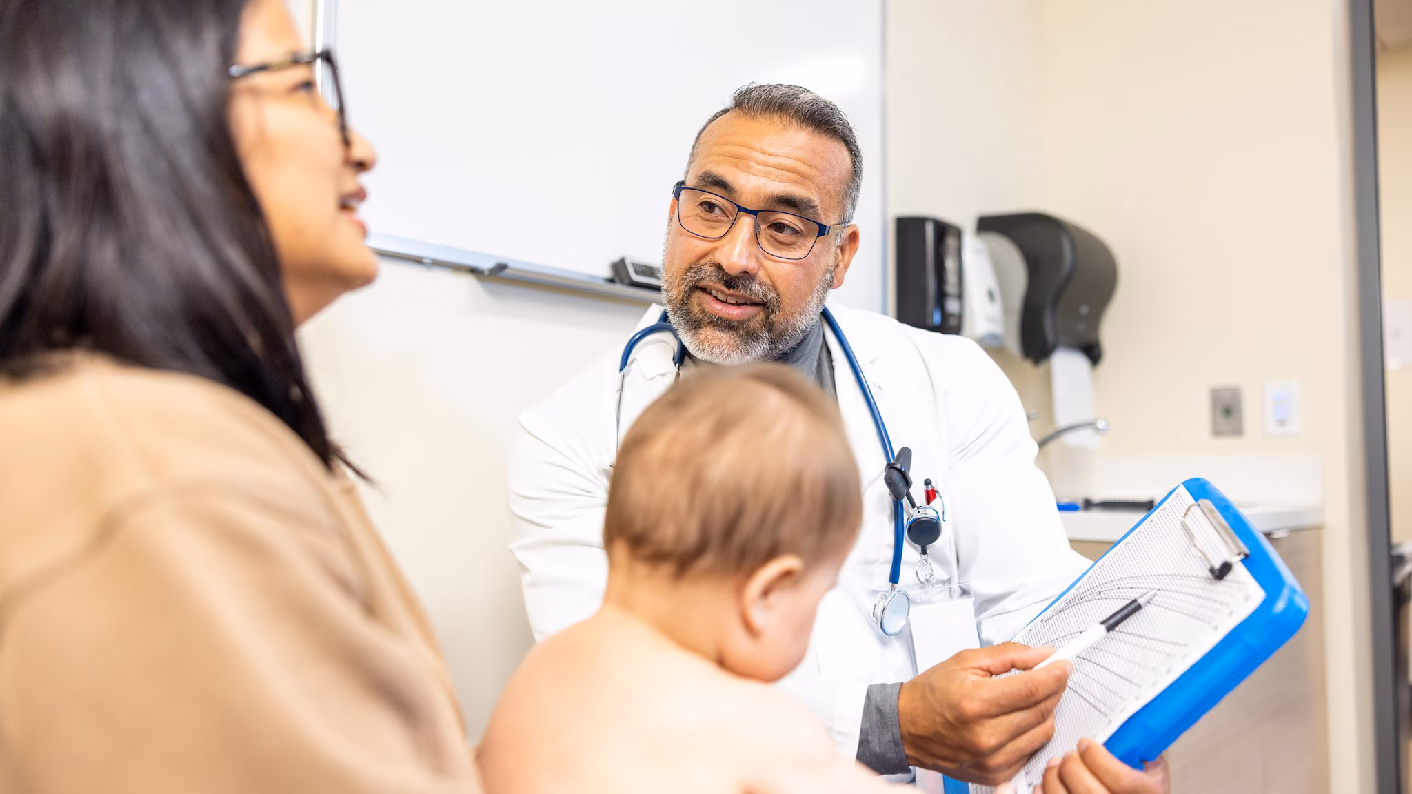 Doctor reviews infant growth chart Doctor reviewing infant growth chart with a mother who is holding young child on her lap.