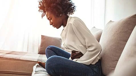 Woman with stomach ache Woman sitting on a couch holding her stomach with her eyes closed and a pained look on her face