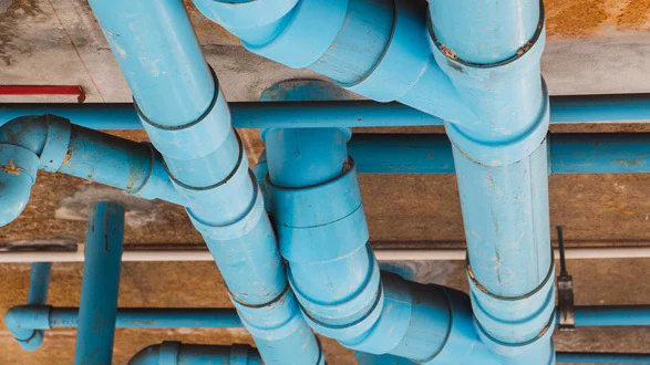 Resized image of pipes Blue pipes running in different directions at the top of an unfinished ceiling inside a building.
