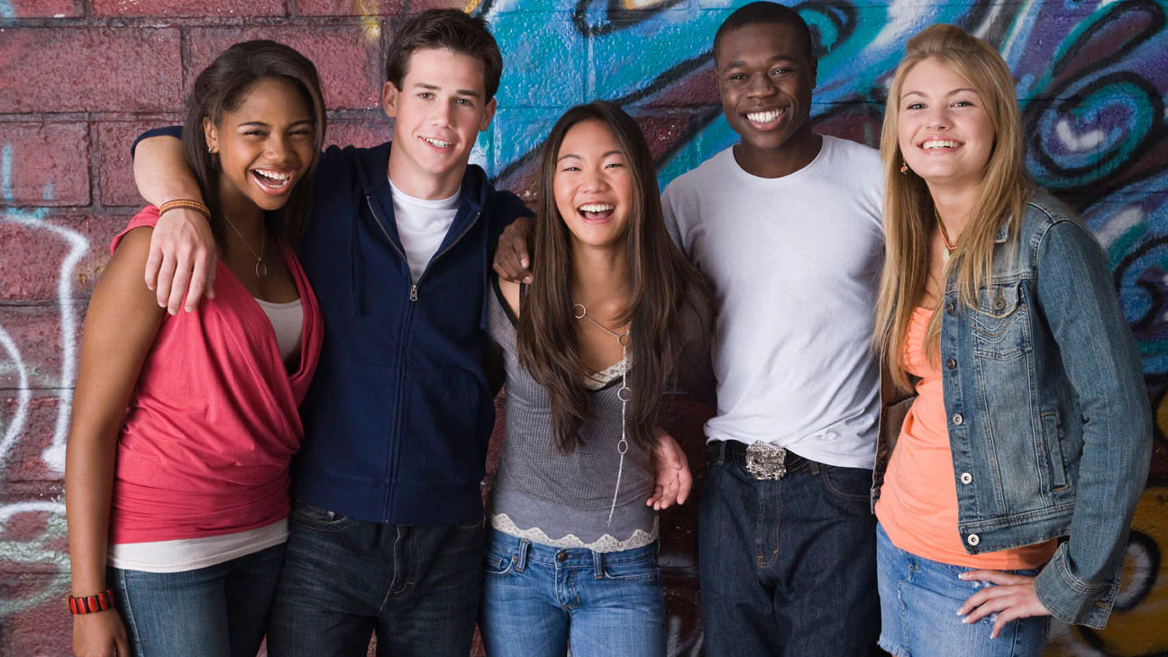 Health Disparities A group of high school students standing together in a classroom, smiling and laughing.