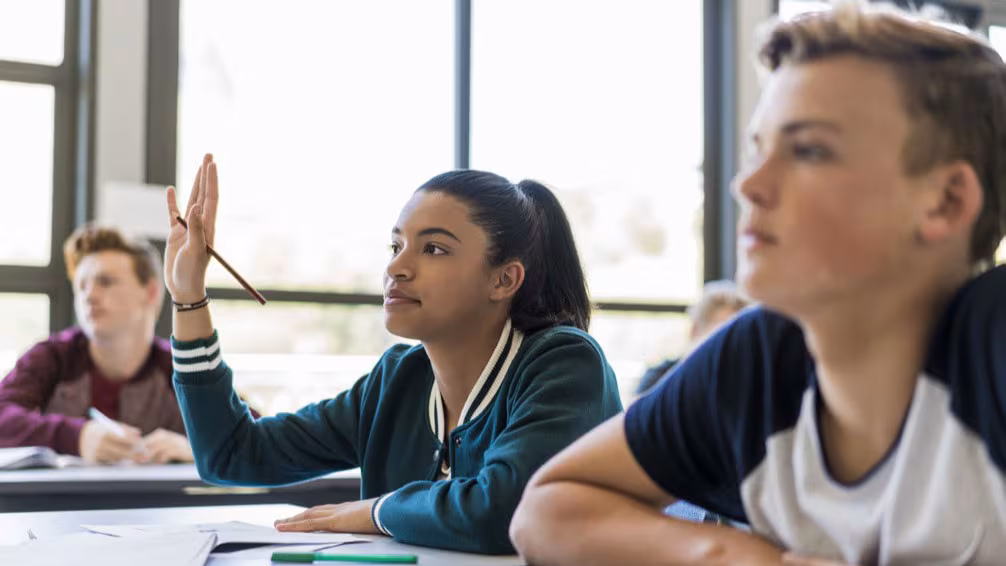 A female high school student raises her hands in classroom.