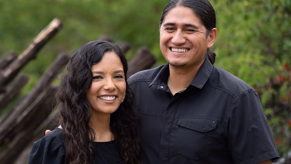 A smiling Native American couple dressed in black shirts.