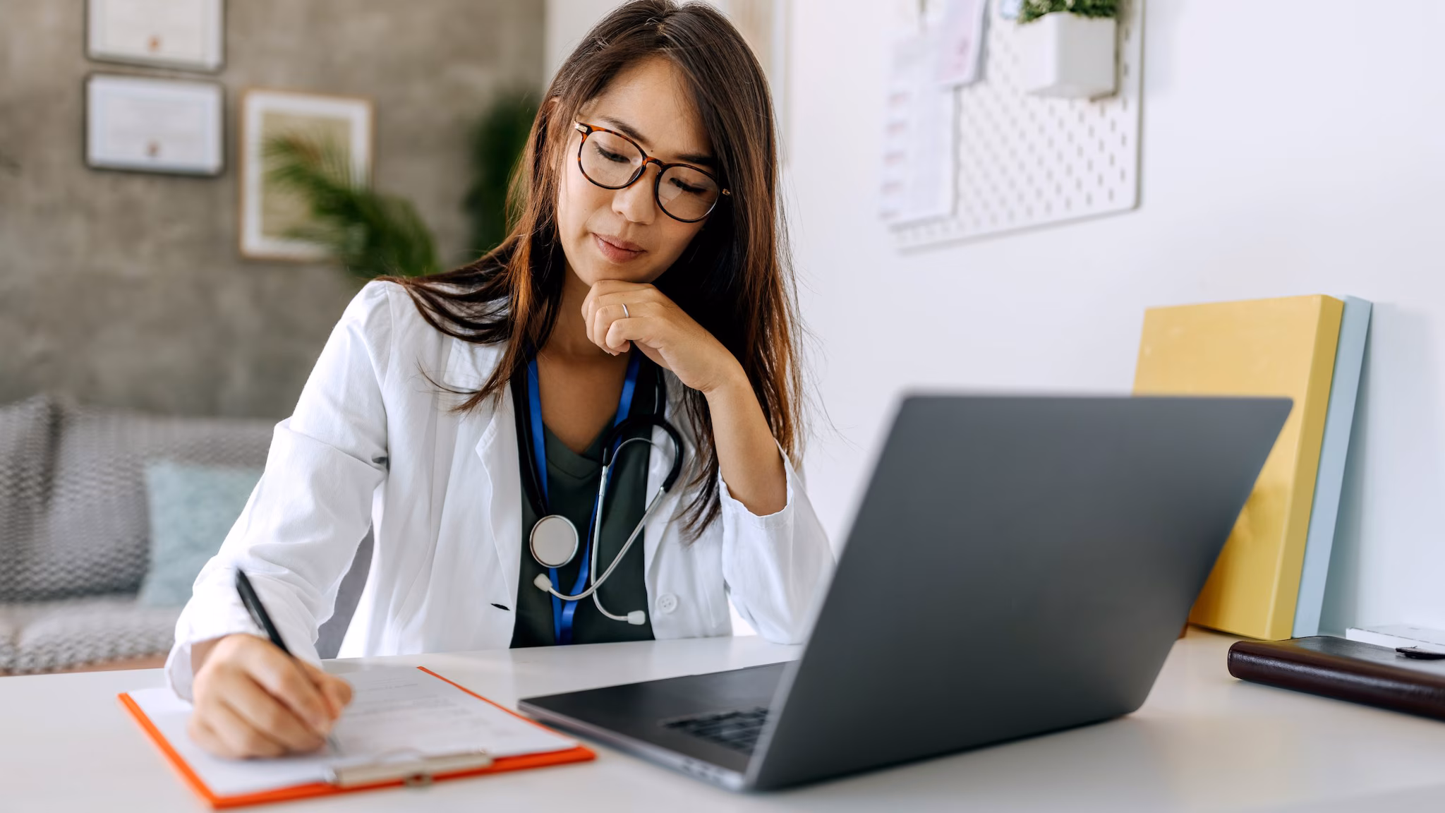 Doctor on computer Healthcare provider takes note on a clipboard next to a laptop.