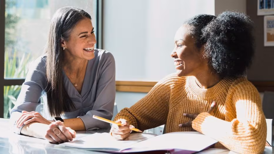 -- title missing -- An adult helping a teenager with schoolwork, as they look at each other and smile.