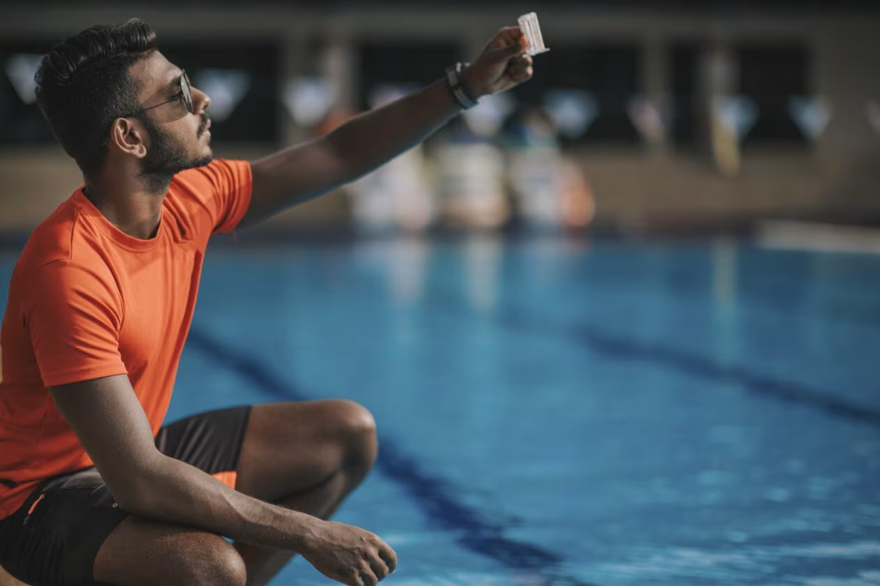 A male lifeguard tests the water at an outdoor pool.
