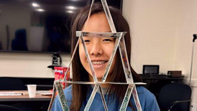Data Detectives Candid Young asian girl stands behind a house triangle formed by balancing playing cards