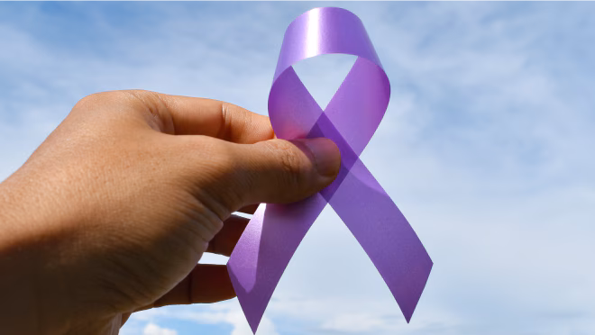 A hand holds a purple ribbon for overdose awareness against a blue sky