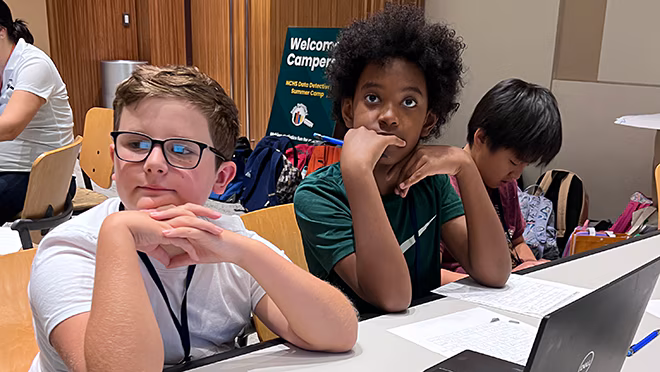 Candid 1 2024 ATL Camp Campers sit at a table, listening intently to an instructor
