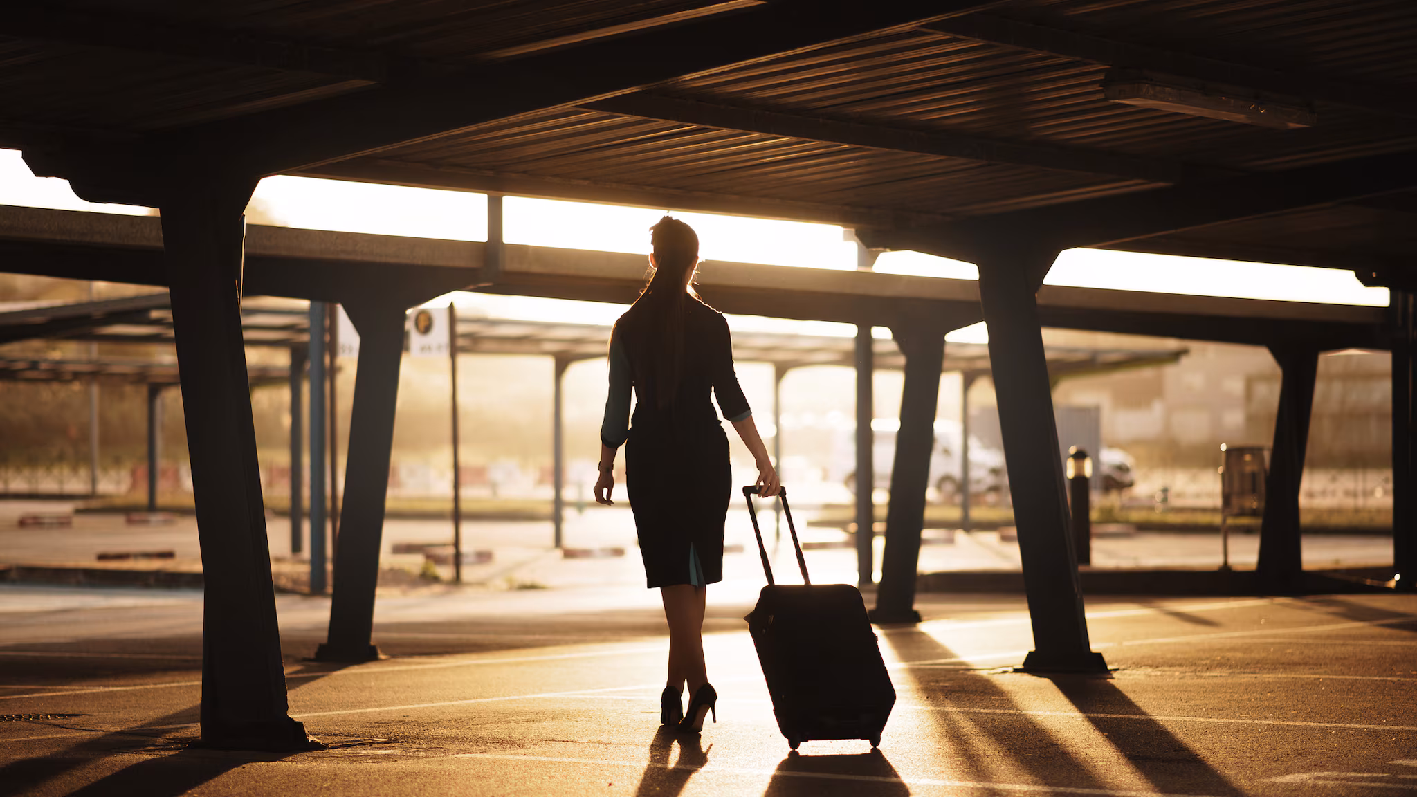 1305054958 Silhouette of an aircrew member with a suitcase at sunset at an airport