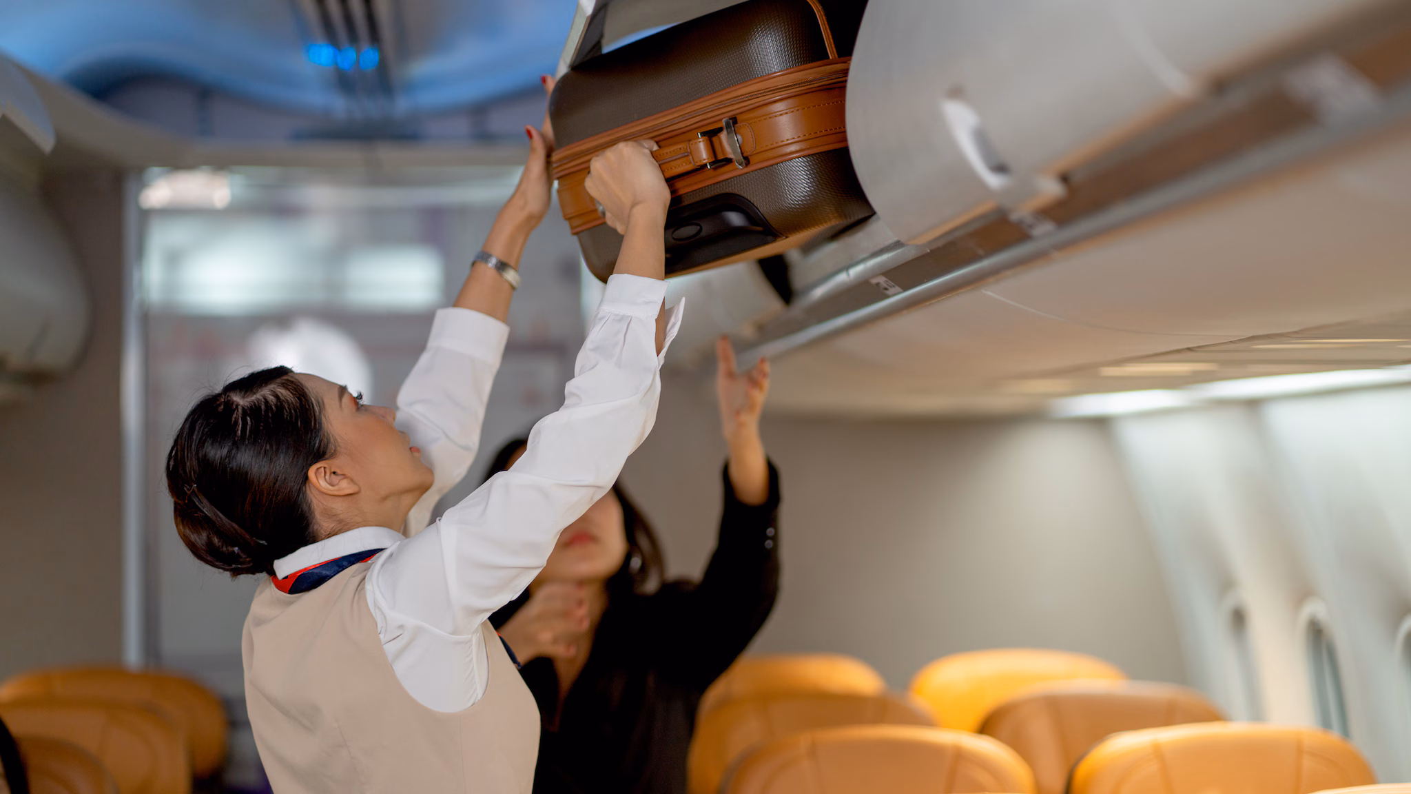 1389718346 Aircrew members securing carryon baggage in an overhead compartment.