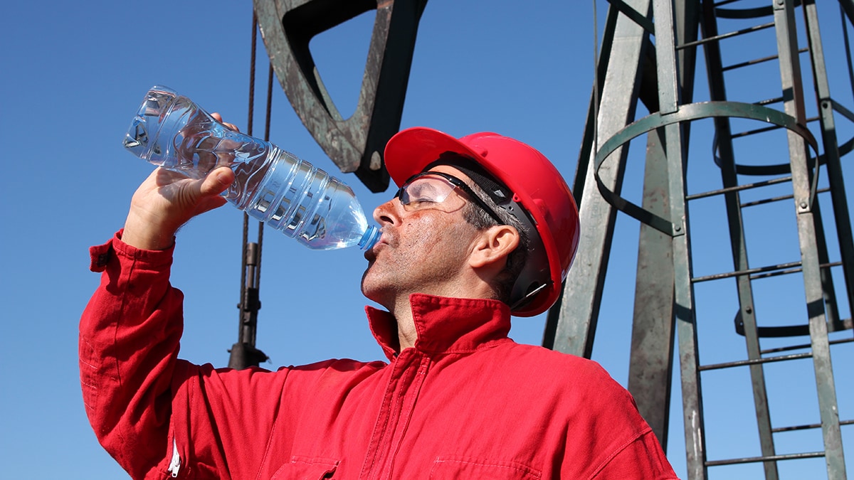 Heat Stress Construction worker wearing a red jacket and red hard hat drinking water