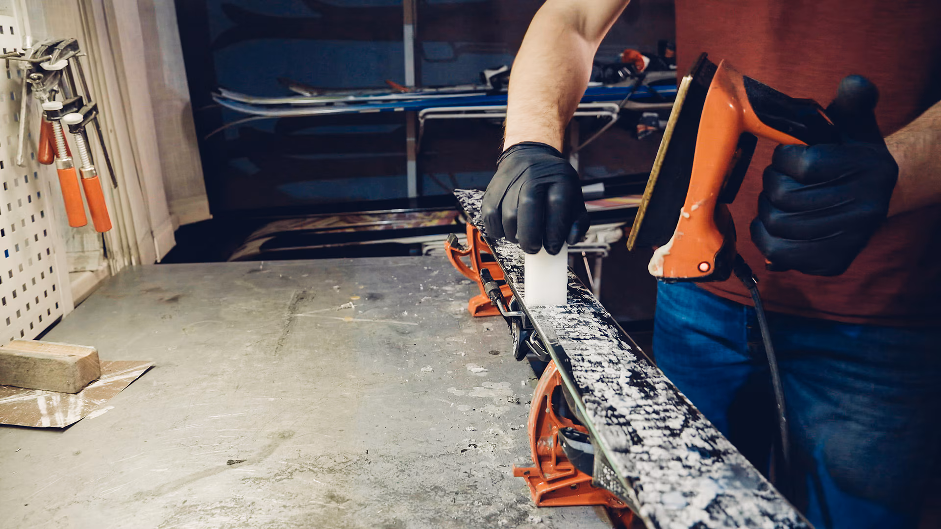 1196415915 A worker waxing a ski on a bench.