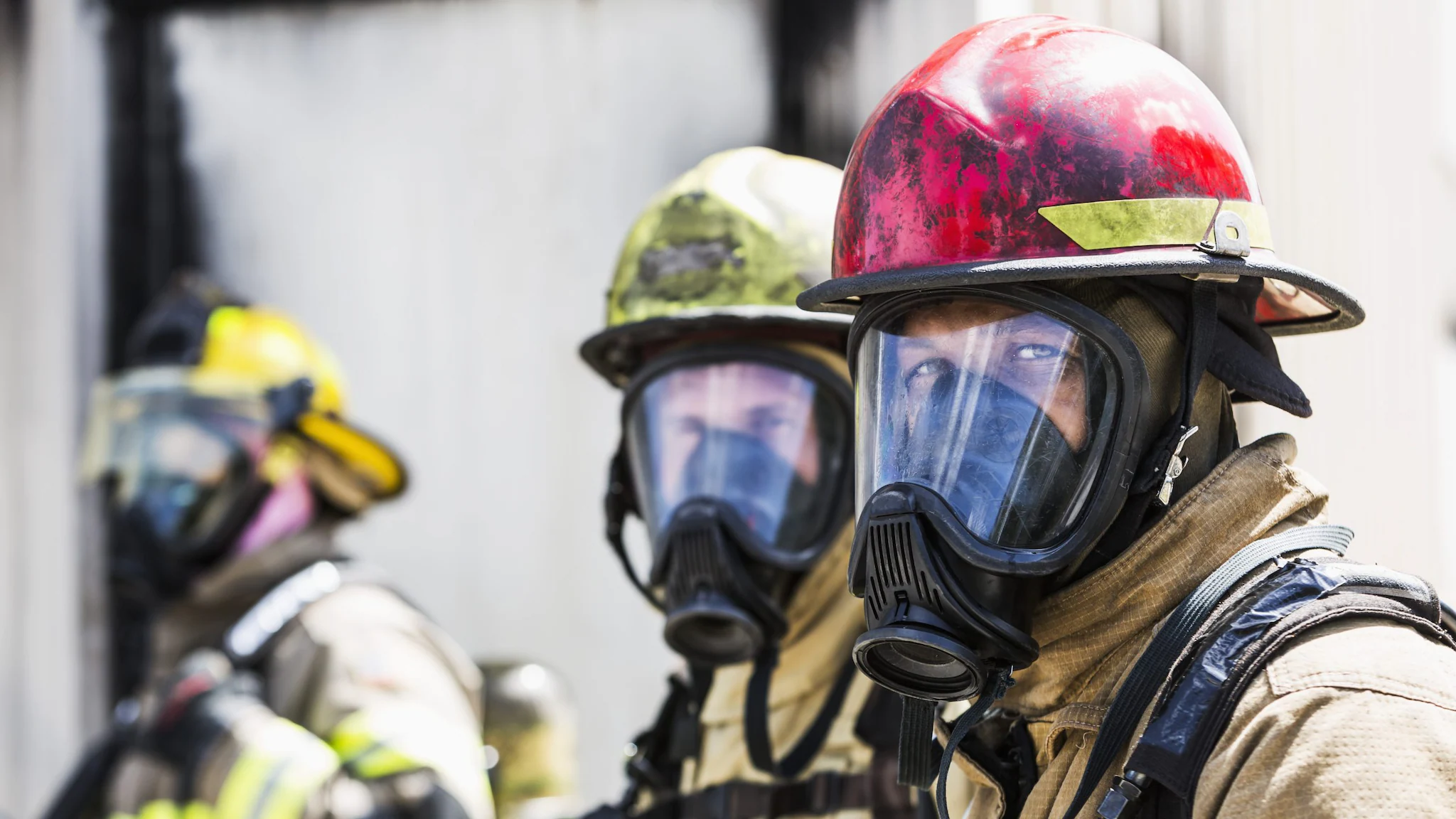 Front Facing Firefighter PPE Three firefighters wearing personal protective equipment. Front two firefighters are looking into camera.
