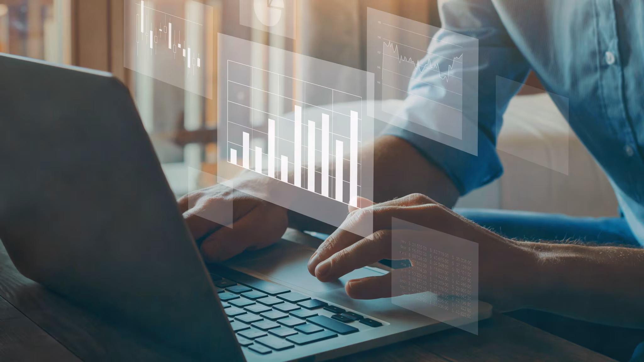 Hands typing on a laptop with small, transparent charts and graphs.