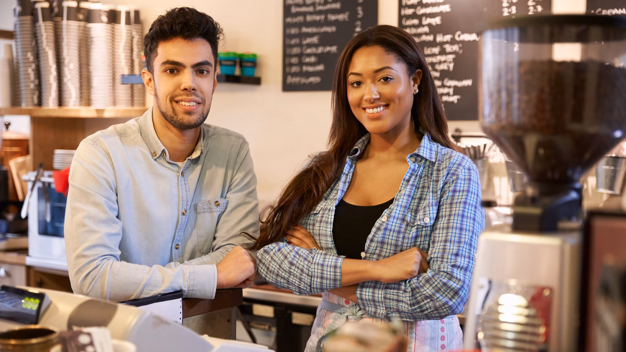 Male and female young workers standing behind coffee shop counter.