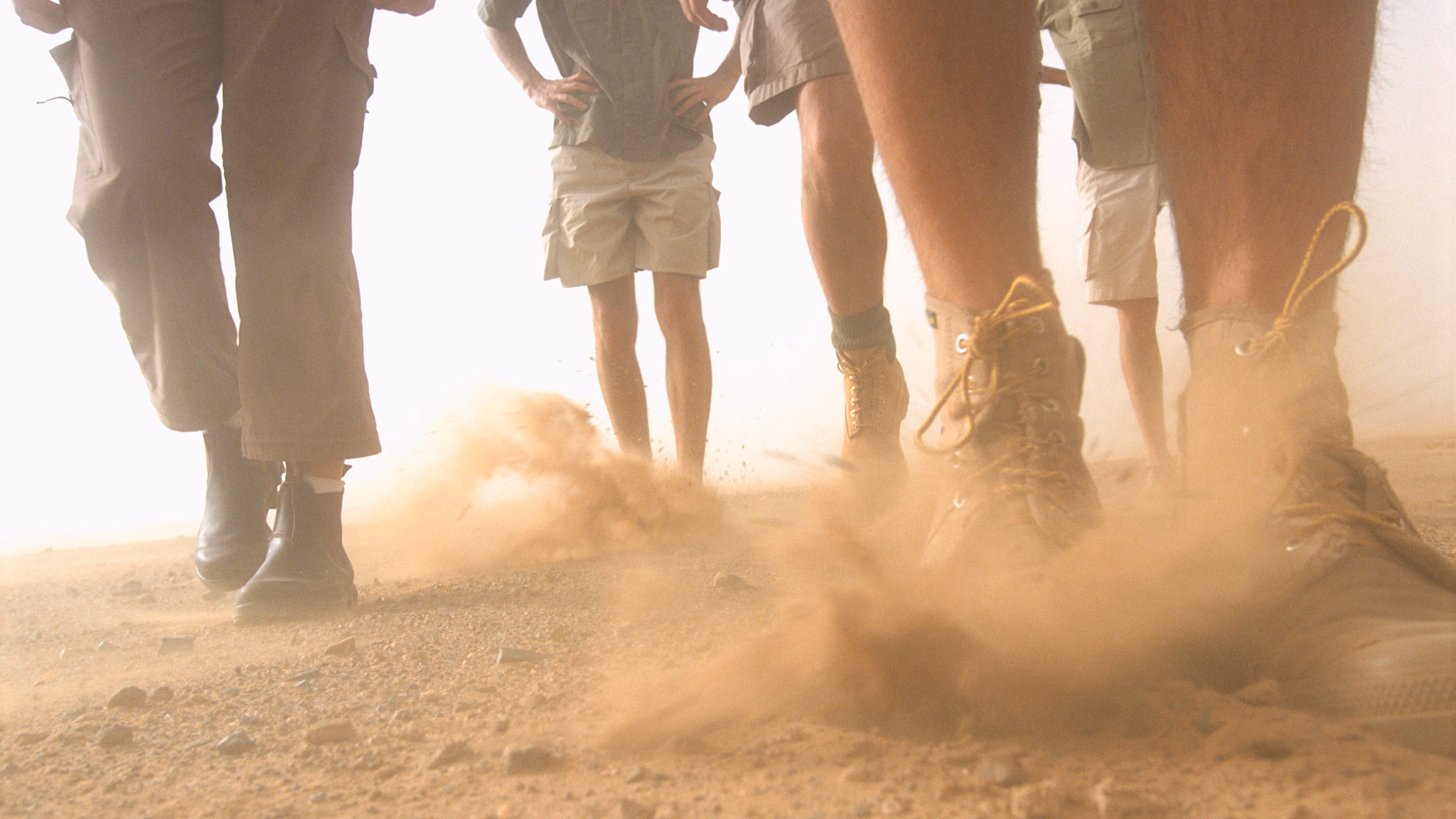 — title missing — Photo of people's legs walking on dusty soil.