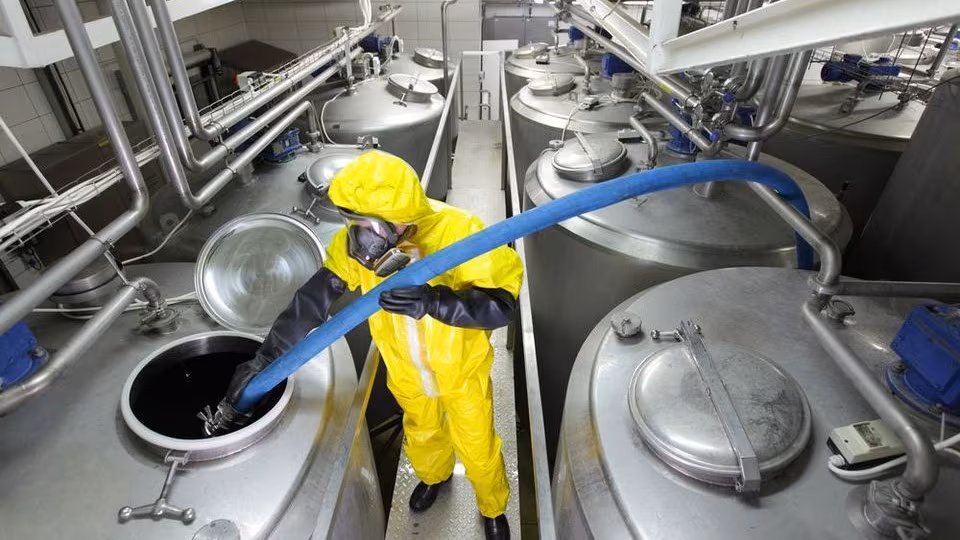 Chemical manufacturing worker chemical manufacturing worker in a yellow suit handling chemicals in a large steel canister