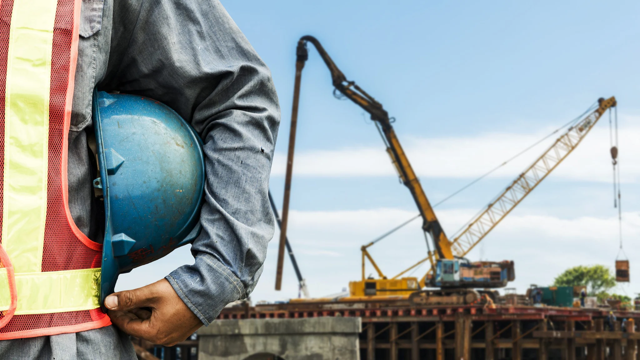 — title missing — Man holding a blue construction hat with a crane in the background