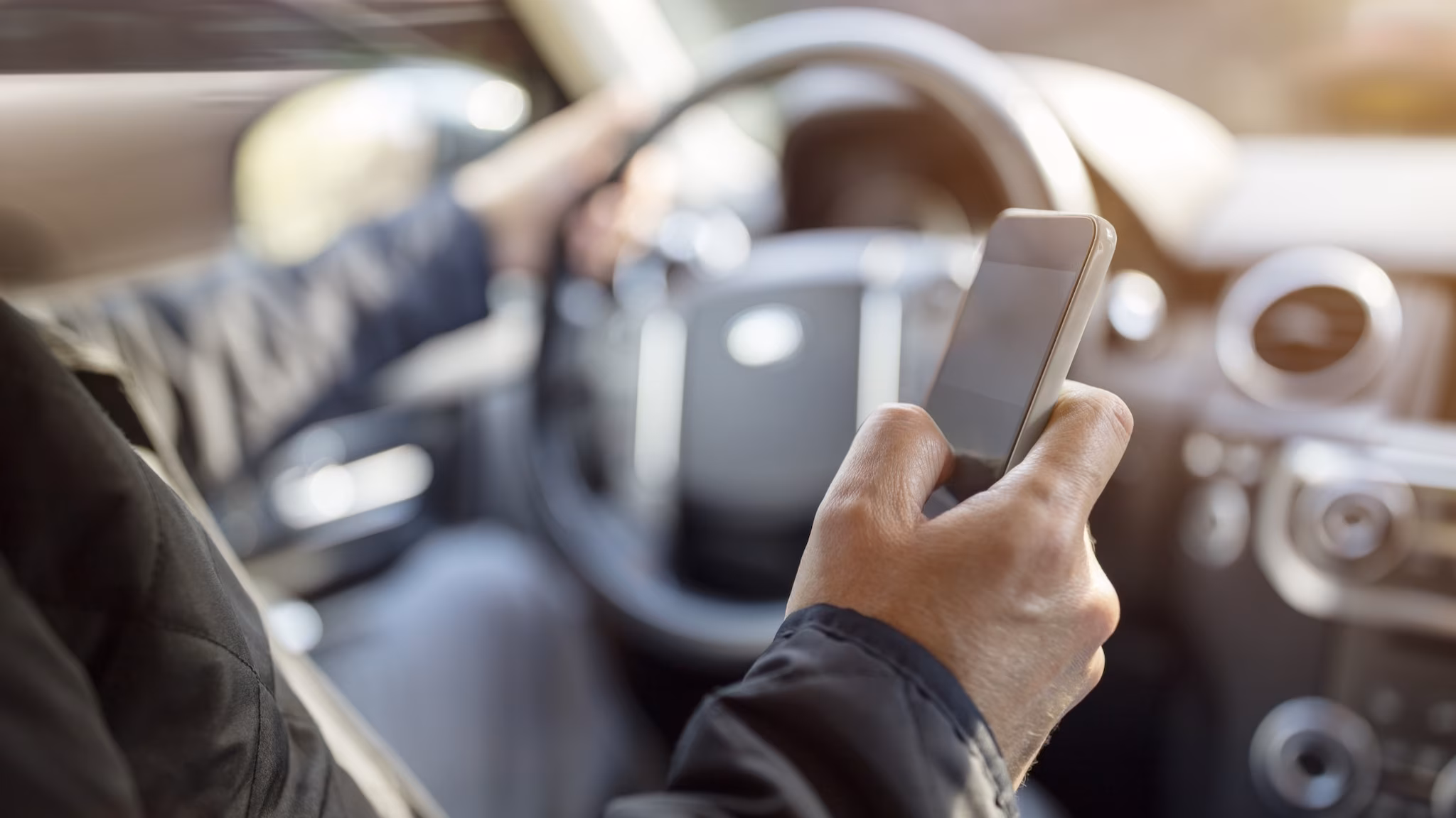 Driver with one hand on wheel and the other hand using a cell phone