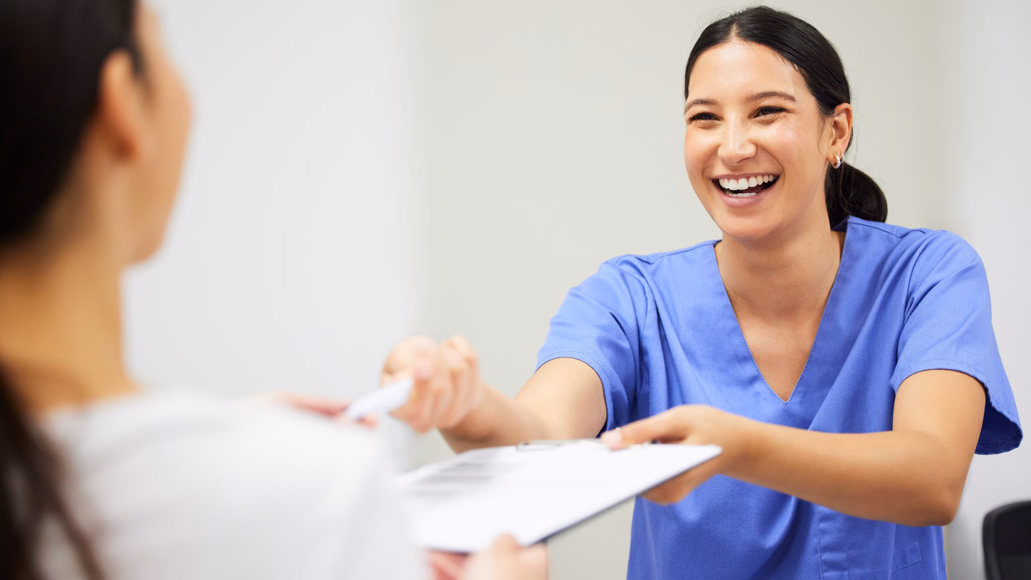 smiling woman wearing blue scrubs passing a piece of paper to another person
